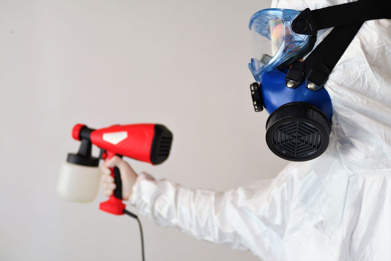 services-02 A worker in protective gear uses a disinfectant spray indoors.